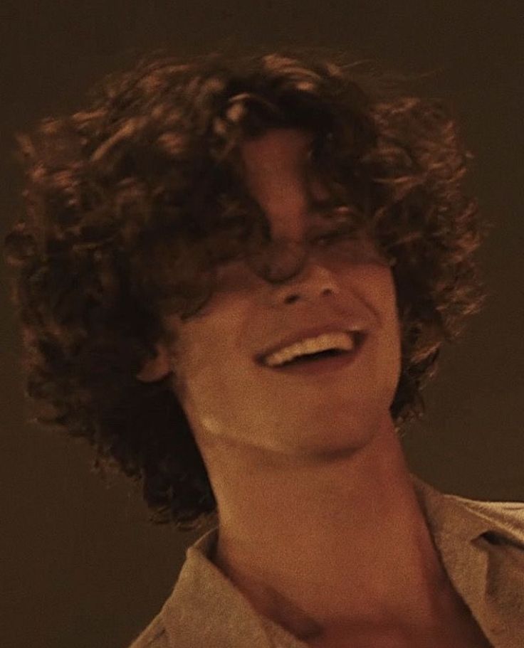 a man with curly hair smiling at the camera