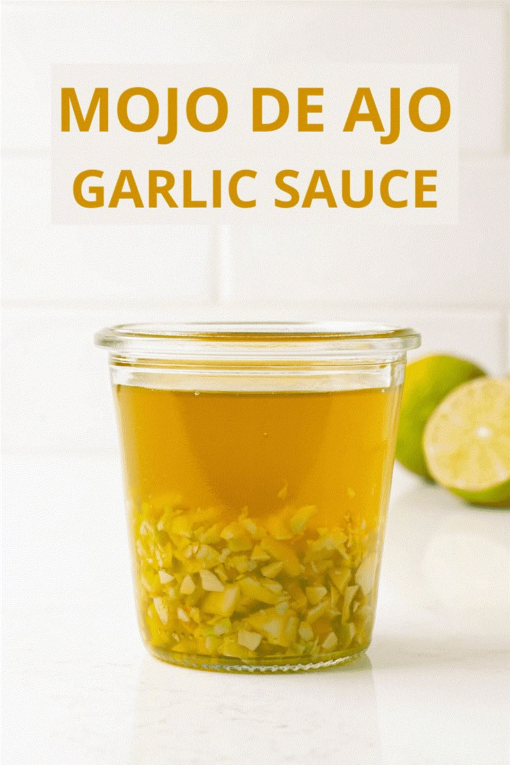 a glass jar filled with garlic sauce next to limes on a white counter top