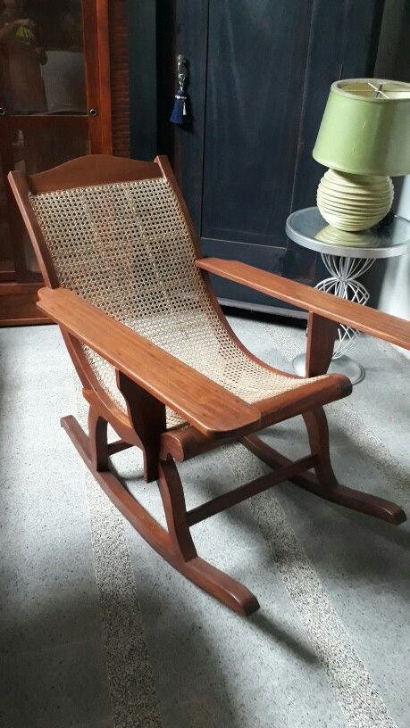 a wooden rocking chair sitting on top of a carpeted floor next to a lamp