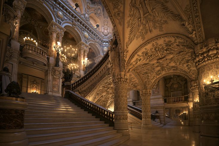 an ornate staircase with chandeliers and lights in a large palace like building that is lit up at night