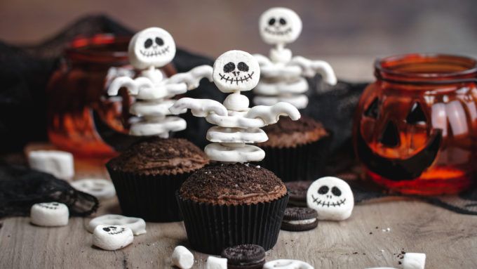 halloween cupcakes with skeleton decorations and candy on the table in front of them