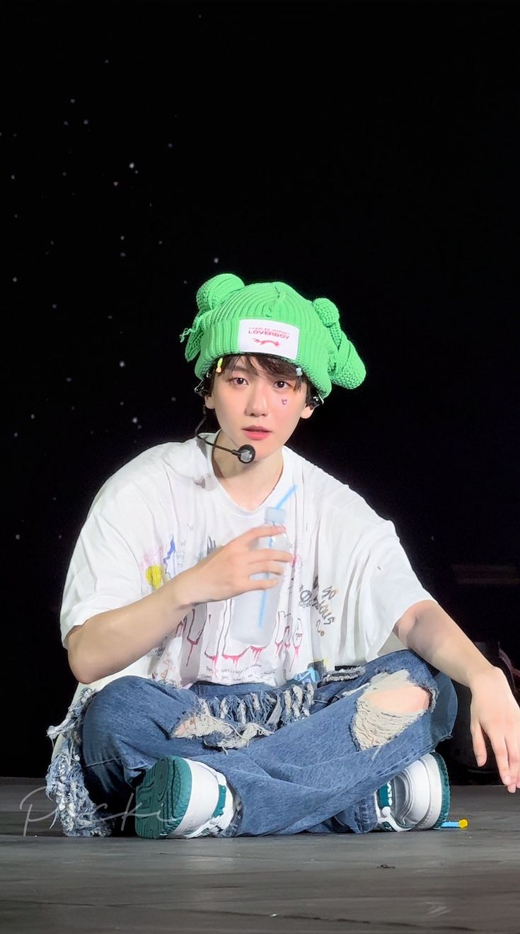 a young man sitting on the floor wearing a green hat