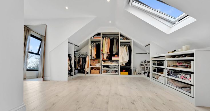 an attic bedroom with white walls and wooden floors, skylights above the walk in closet