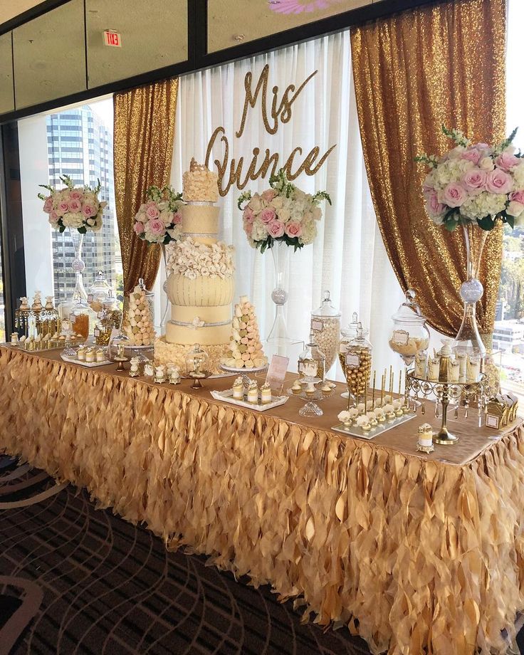 a wedding cake and dessert table in front of a large window with gold drapes