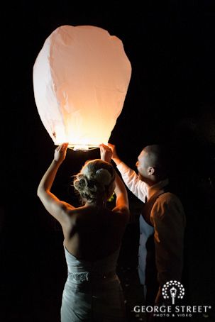 a bride and groom holding up a paper lantern in the dark with their faces illuminated