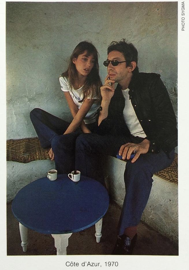 a man sitting next to a woman on top of a blue table in front of a white wall