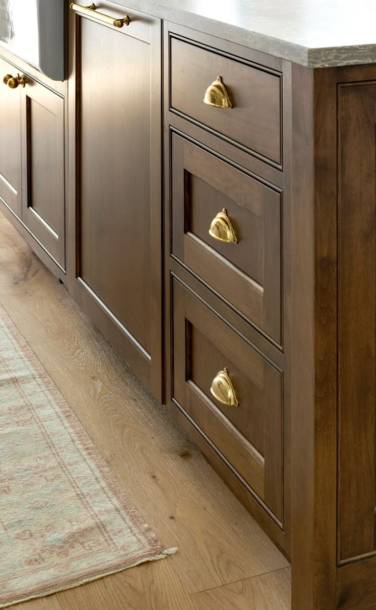 a kitchen with wooden cabinets and gold pulls on the drawers, along with a rug