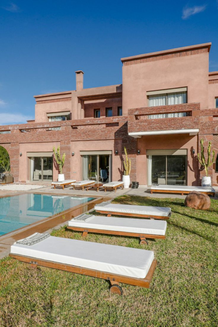 an outdoor swimming pool surrounded by lawn furniture and cactus in front of a large brick building