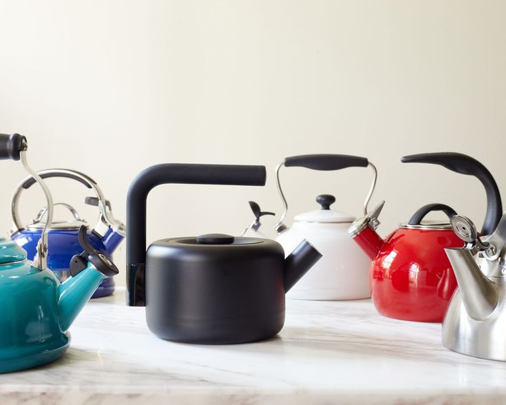 four tea kettles are lined up on a marble counter top, one is blue and the other is red