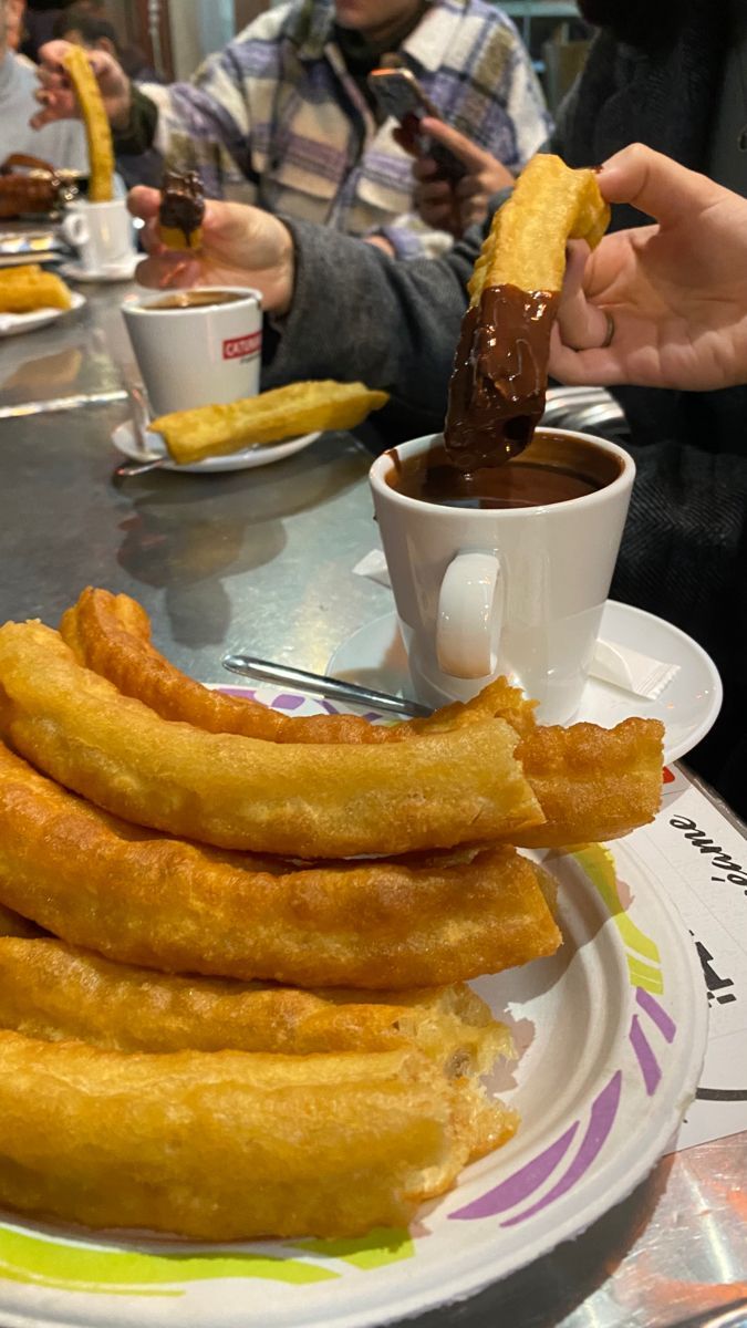 some fried food is on a plate with dipping sauce in the middle and people sitting at a table behind it