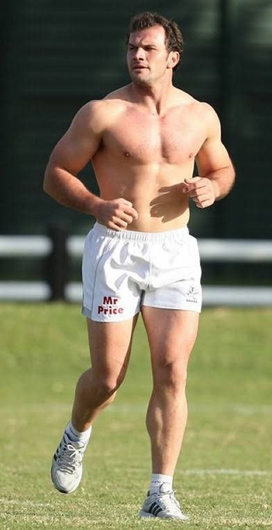 a shirtless man running in the grass with his hands on his hips while wearing white shorts