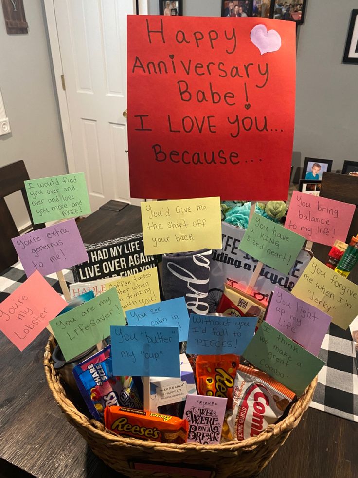 a basket filled with lots of different types of candy and notes on the table next to a sign that says happy anniversary babe i love you because