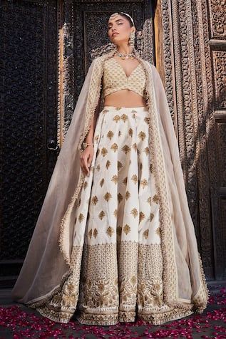 Ivory silk lehenga with an attached cancan and gold floral embroidery. Comes with a padded blouse and a dupatta.
Components: 3
Pattern: Embroidered
Type Of Work: Floral
Neckline: Deep V Neck
Sleeve Type: Sleeveless
Fabric: Silk
Color: Ivory
Other Details: 
Attached lining
Product Weight: 2 Kgs
Occasion: Wedding - Aza Fashions Festive White Raw Silk Gown, White Lehenga With Sheer Dupatta In Raw Silk, White Lehenga With Zari Work For Ceremonies, Organza Sharara With Gold Embroidery For Reception, White Lehenga With Pallu For Ceremony, Gold Embroidered Tissue Silk Traditional Wear For Wedding, Wedding Traditional Wear With Gold Embroidery On Tissue Silk, White Raw Silk Lehenga With Sheer Dupatta, Reception Sharara With Gold Embroidery In Raw Silk