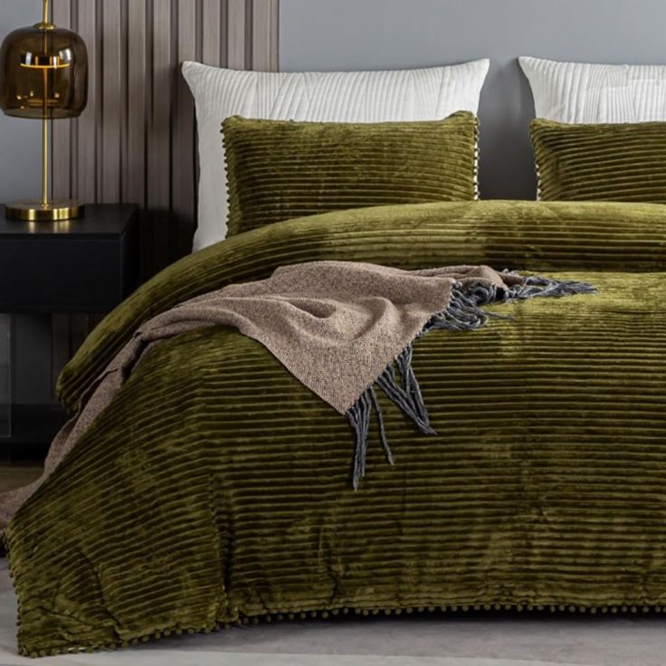 a bed with green bedspread and pillows on top of it next to a night stand