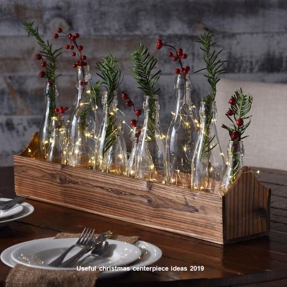 a wooden table topped with lots of glass bottles filled with christmas lights and greenery