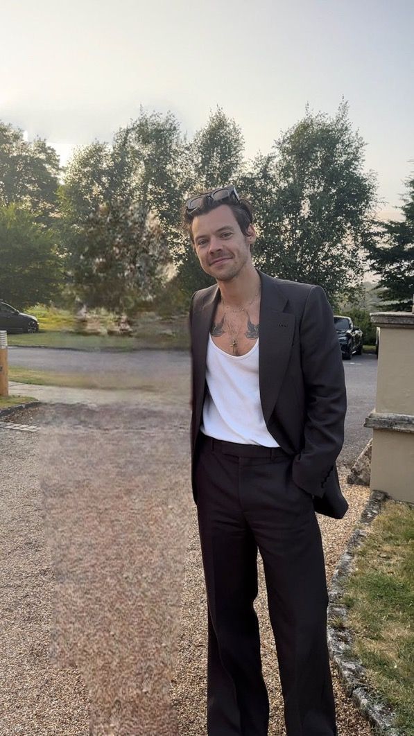 a man in a black suit and white t - shirt is standing on the street