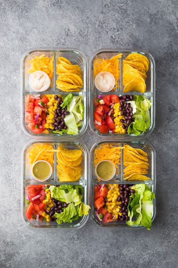 four plastic containers filled with salads and dressing on top of a gray countertop