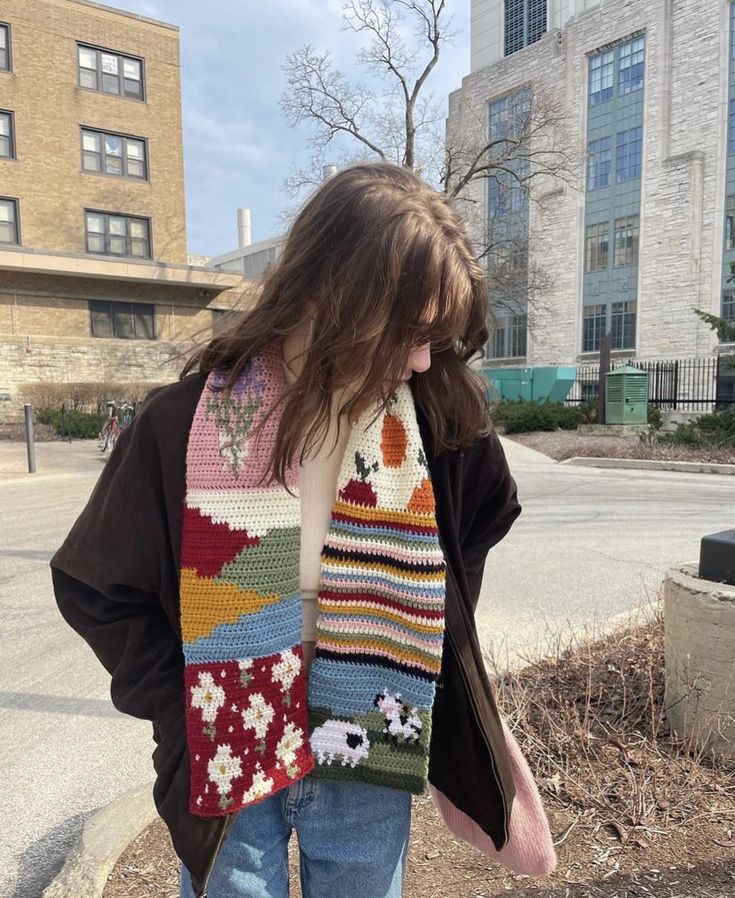 a woman wearing a multicolored crocheted scarf standing in front of a building