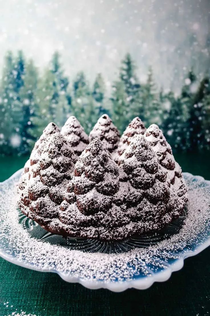 three small cakes on a glass plate covered in powdered sugar with trees behind them