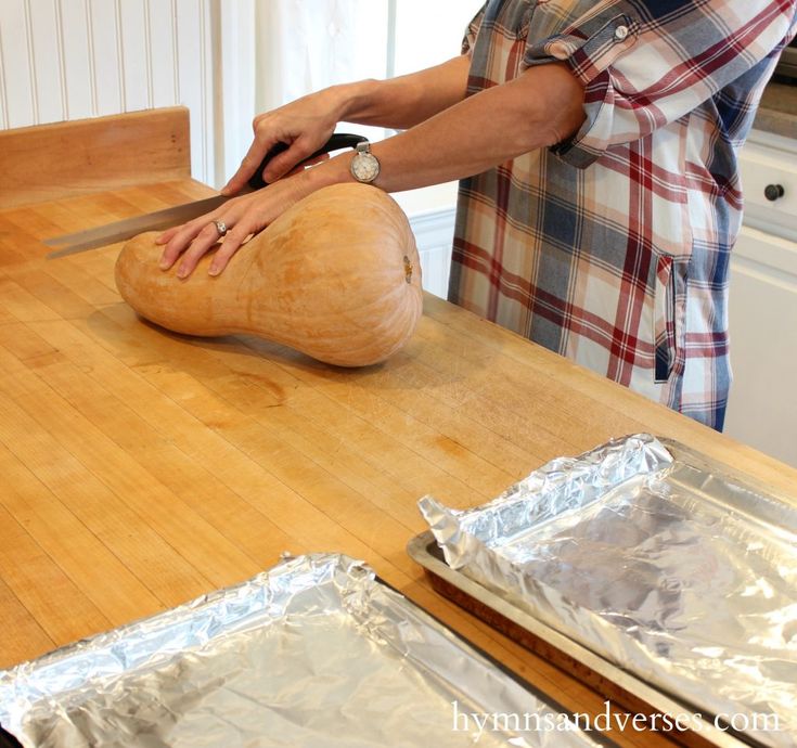 a person cutting bread on top of a wooden table with aluminum foil covering it and another person in the background