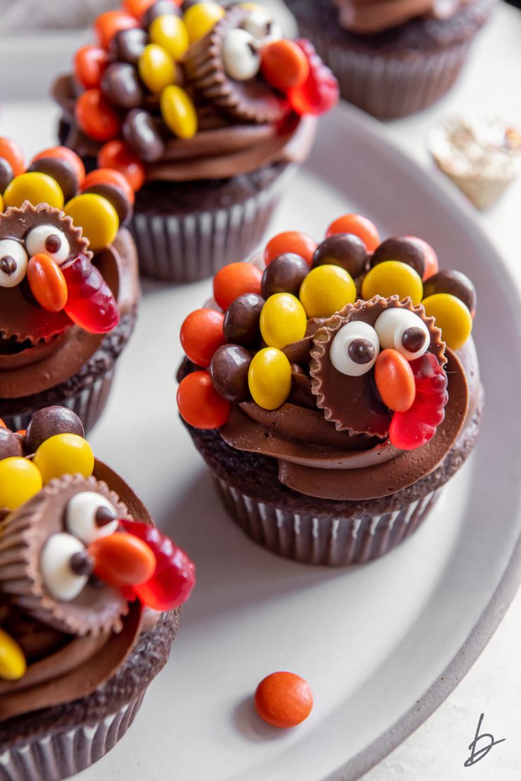 cupcakes with chocolate frosting decorated as turkeys and candy candies on a white plate