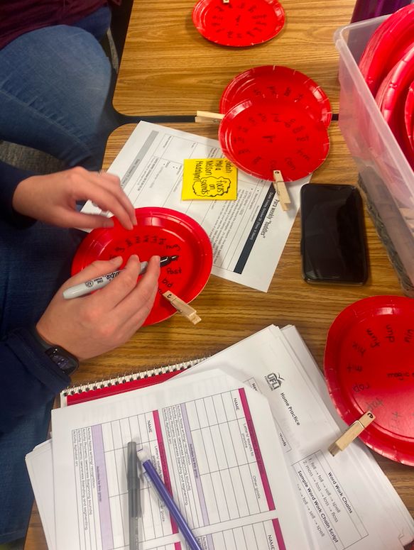 two people sitting at a table with red plates and papers on it, one person is writing