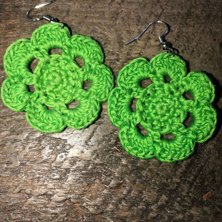 two green crocheted flower earrings sitting on top of a wooden table