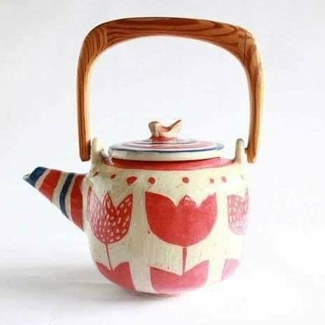 a tea pot with a wooden handle and birds on the top, sitting on a white surface