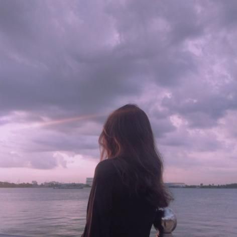 a woman standing on the edge of a boat looking out at the water and clouds