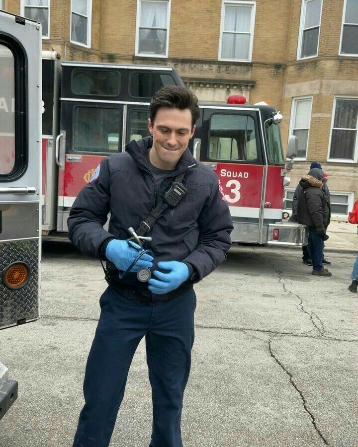 a man in blue gloves standing next to a firetruck and smiling at the camera