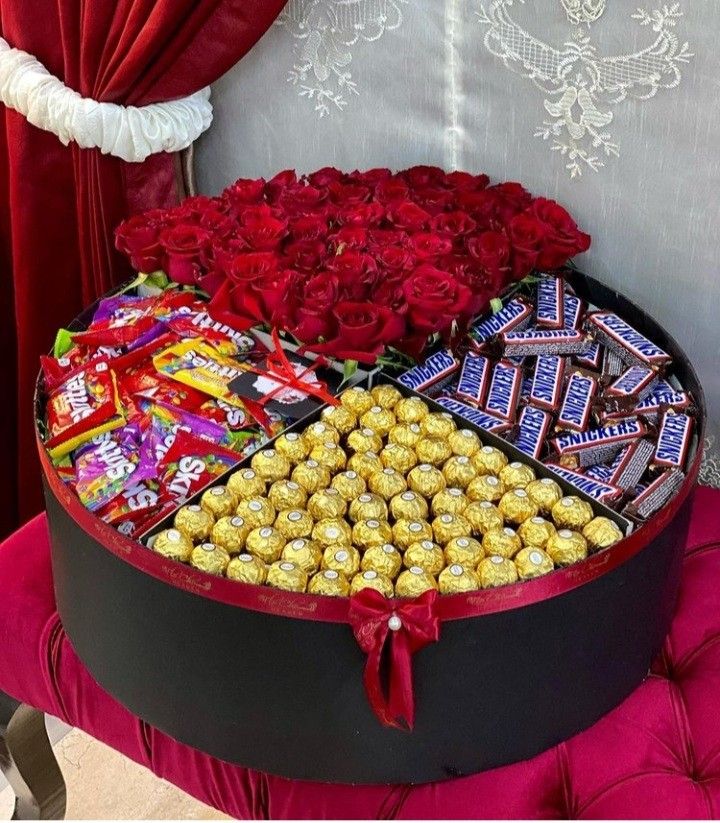 a heart shaped box filled with roses, chocolates and candies next to a red curtain