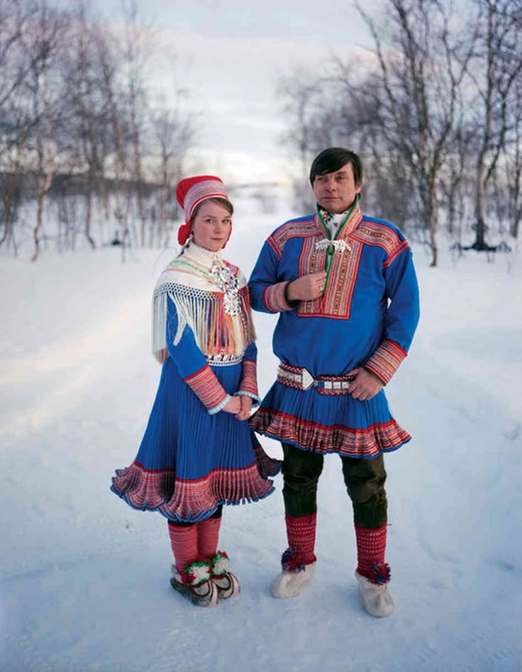 a man and woman dressed in traditional russian clothing posing for a photo on the snow