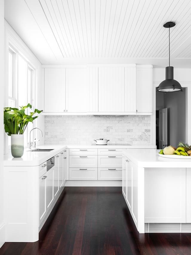 a kitchen with white cabinets and wood flooring next to a potted plant on the counter