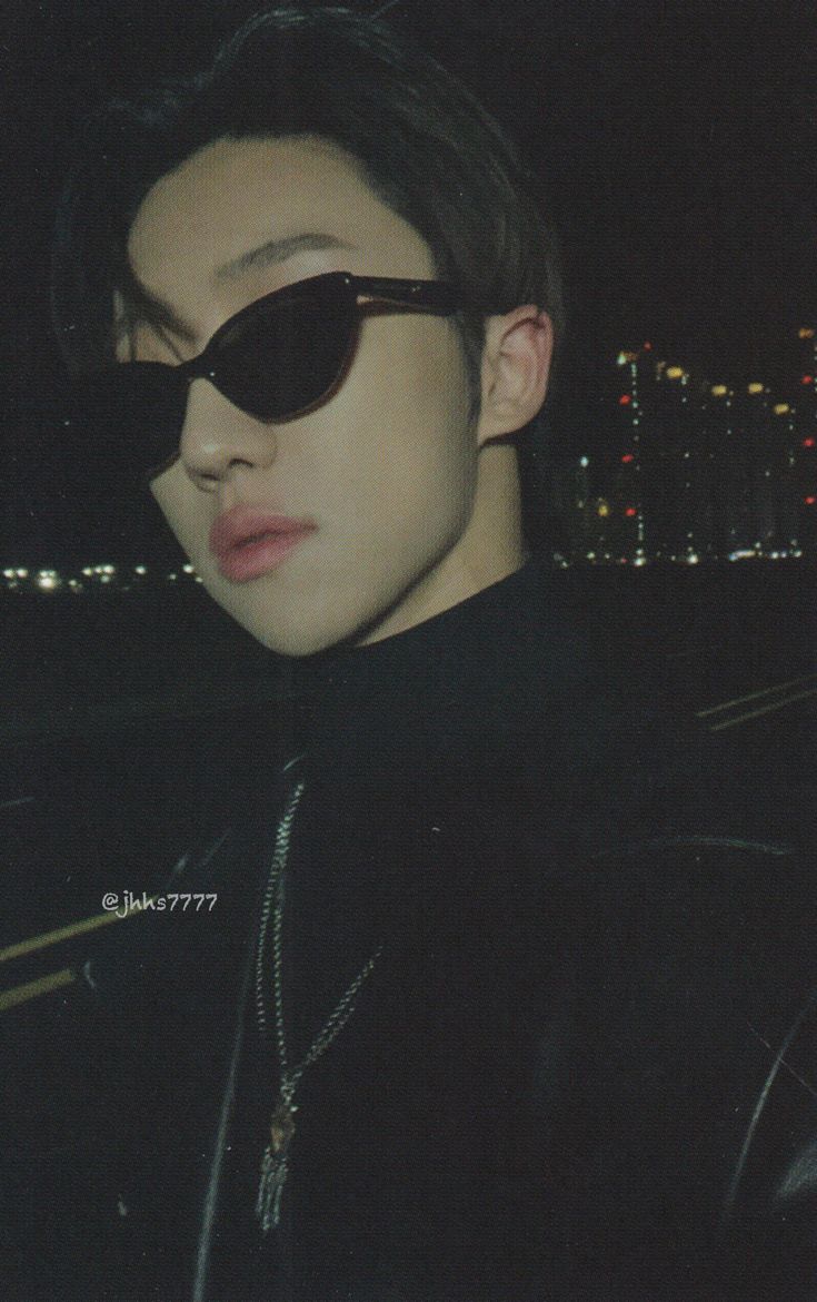 a young man wearing sunglasses in front of a cityscape at night with the sun shining on his face