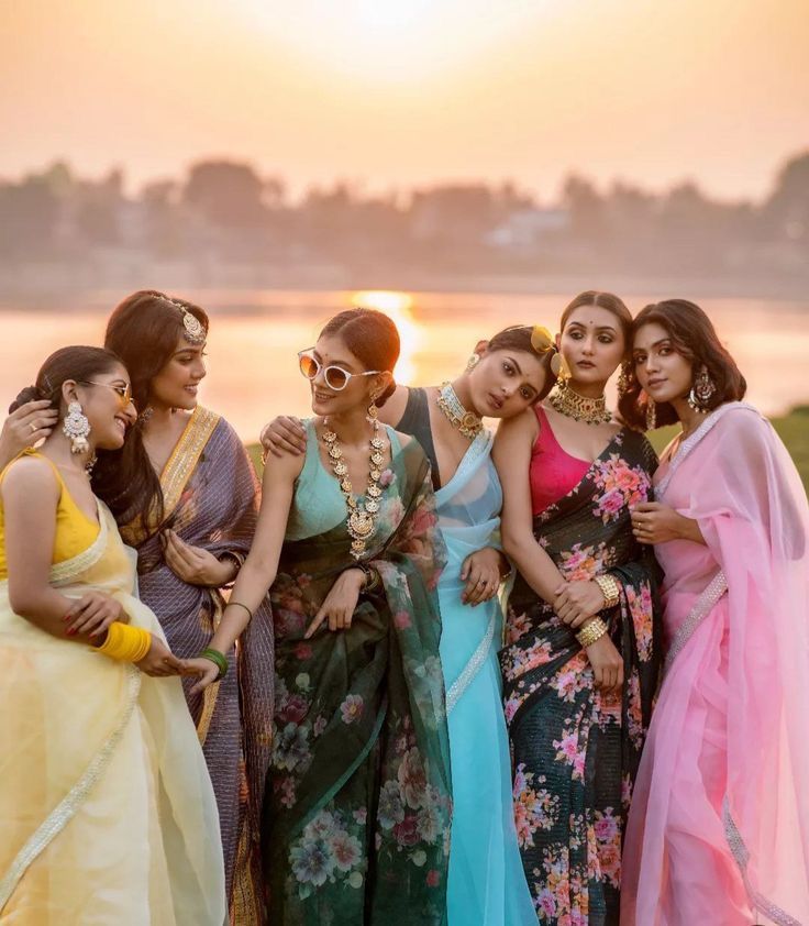 several beautiful women standing next to each other near the water in sari dresses at sunset