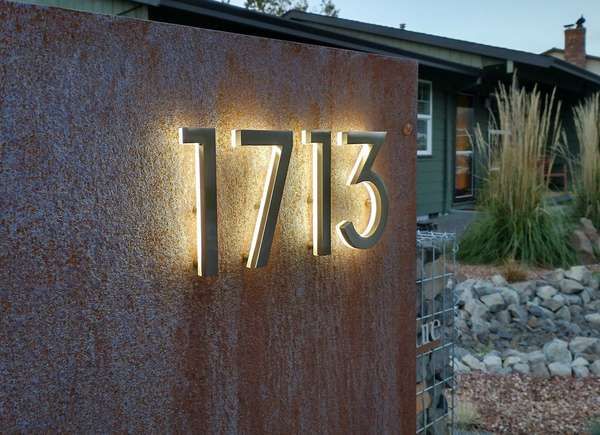 a house number sign on the side of a building with grass and rocks around it