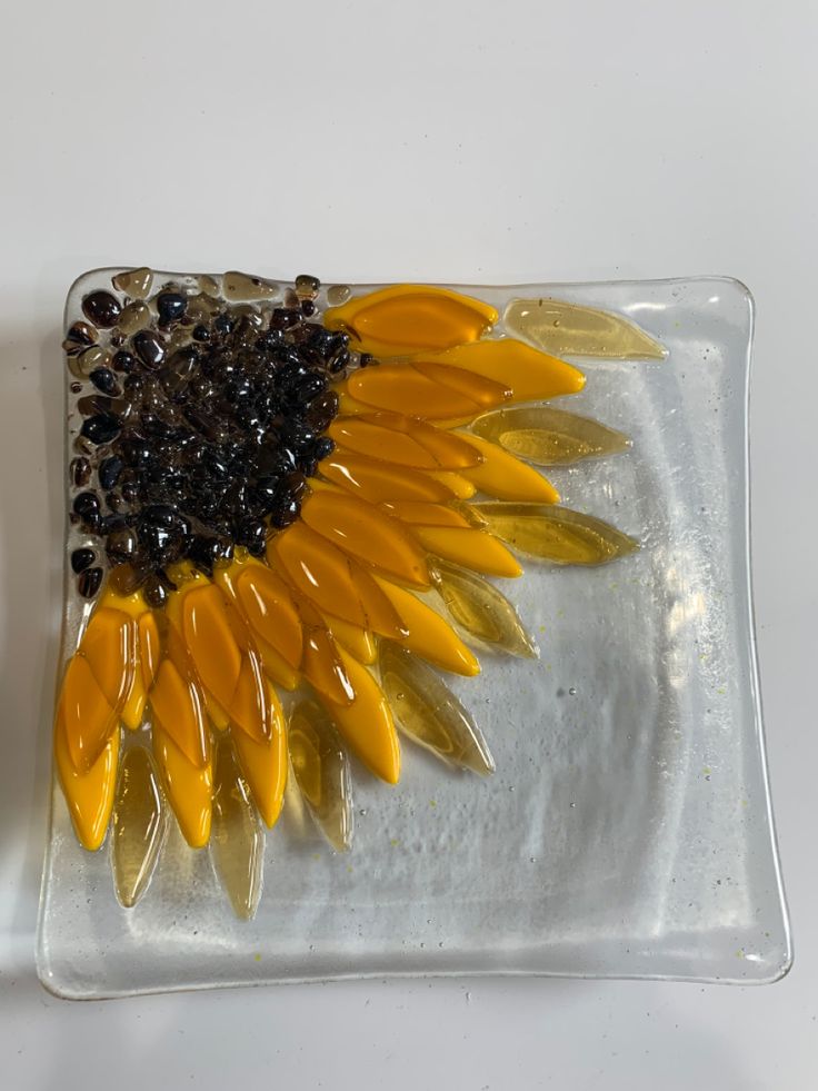 a glass plate with a yellow sunflower on it and some black beads in the middle