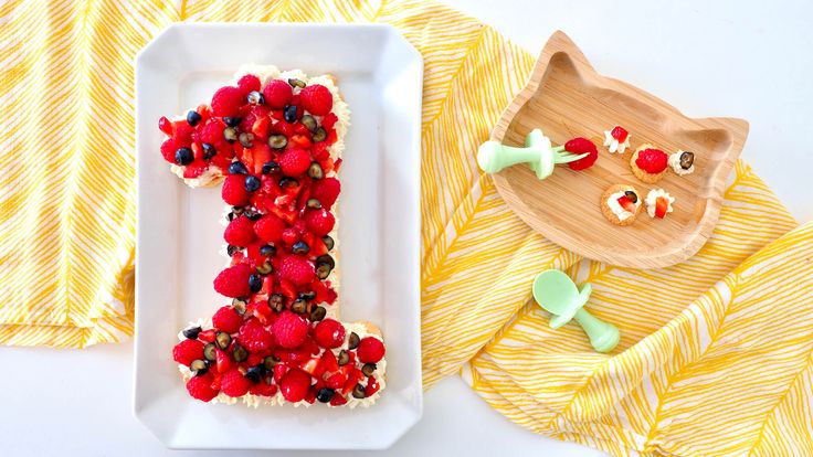 a cake shaped like the letter j with berries on it and a wooden plate next to it