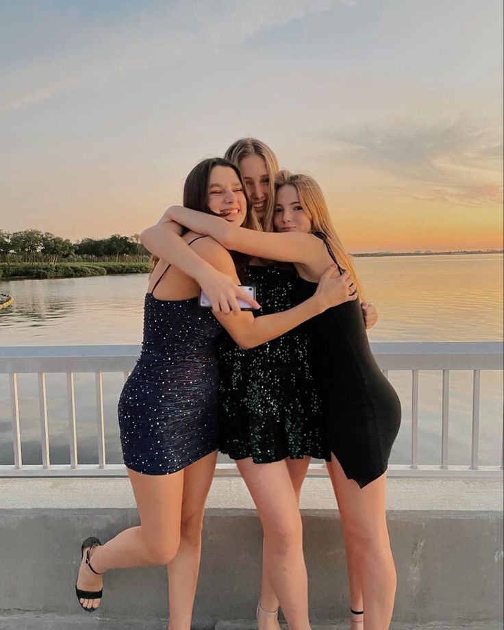 three young women hugging each other while standing next to the water at sunset or sunrise