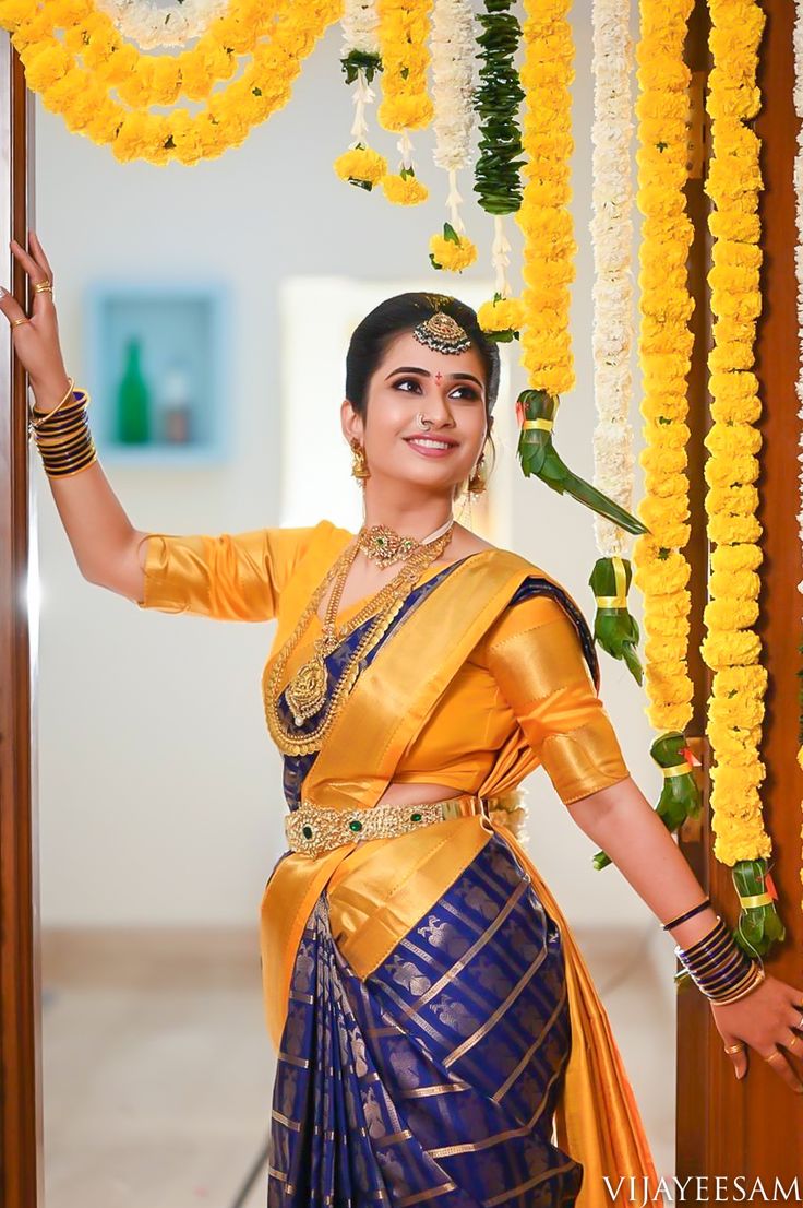 a woman in a yellow and blue sari posing for the camera with her hands up