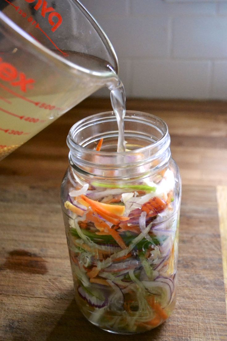 a person pours water into a jar filled with vegetables and vegtables