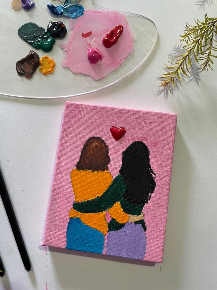 two women hugging each other on a pink canvas next to some paintbrushes and flowers