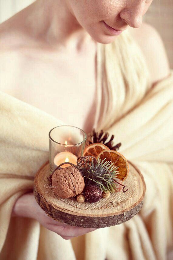 a woman holding a candle and some fruit on a wooden tray with pine cones, an orange slice and cinnamons