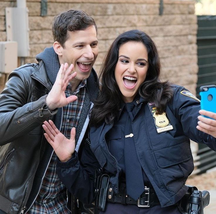 a man and woman standing next to each other holding up their cell phones in front of them