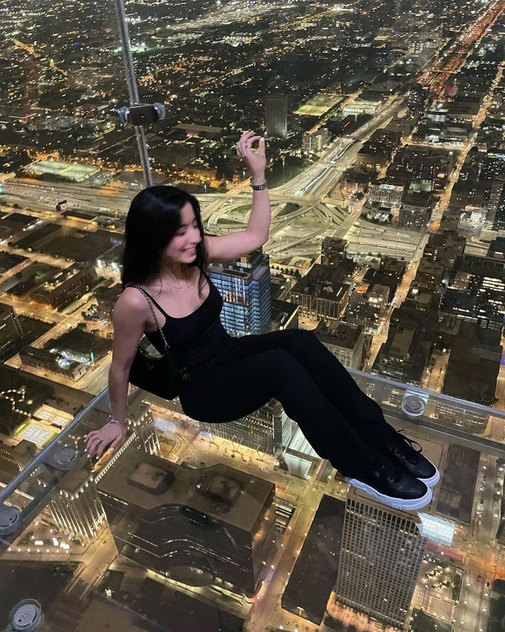 a woman hanging from the side of a tall building with her hands in the air