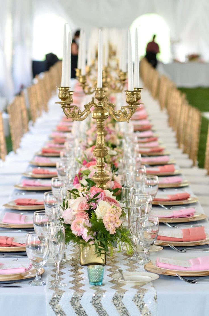 a long table is set with pink and white flowers, gold candelabra, and candles