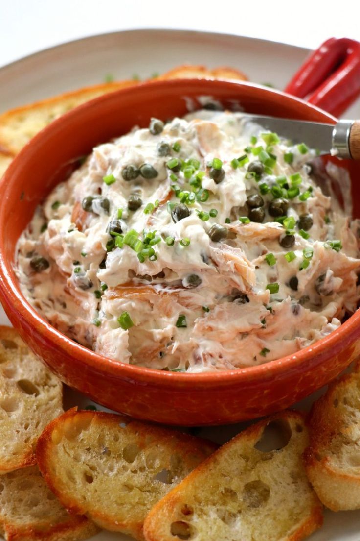 a red bowl filled with food on top of a white plate next to crackers