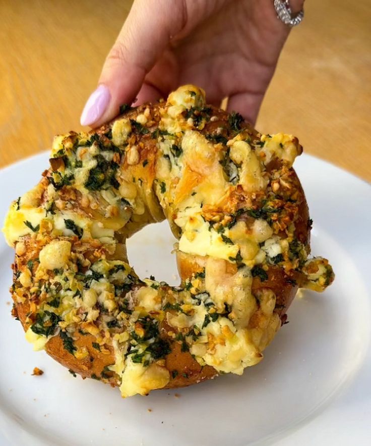 a person is holding up a bagel covered in cheese and spinach on a white plate