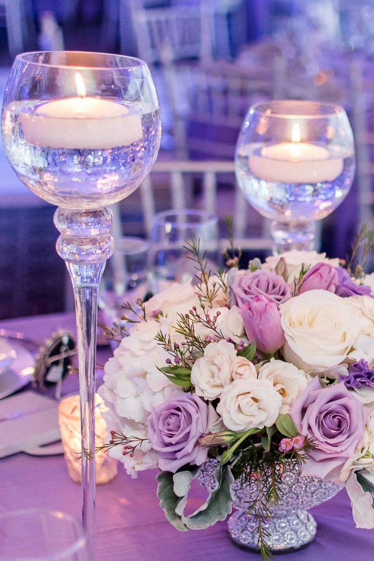 the centerpieces on this table are filled with white and purple flowers, greenery, and candles