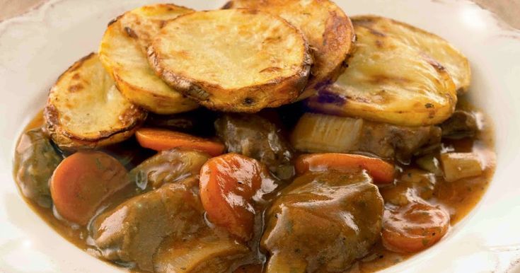 a white bowl filled with meat and vegetables covered in gravy on top of a table